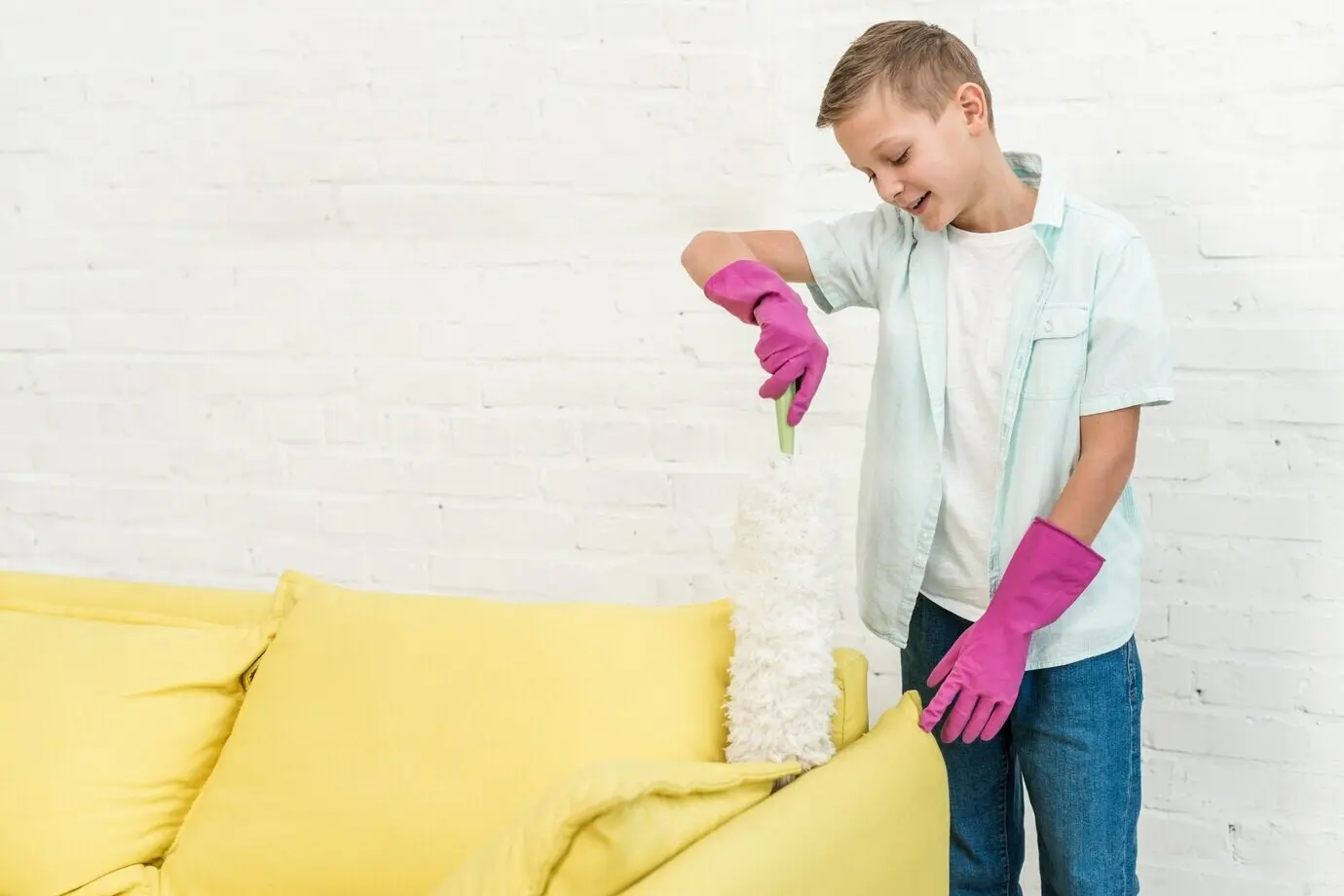 Vorderansicht eines Jungen mit Gummihandschuhen, der einen Staubwedel benutzt.